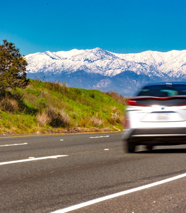 Photo of a car driving on the road with snowy mountains in the background