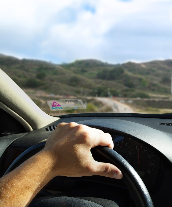 photo of a person gripping the steering wheel of a car with a sticker transponder in the windshield