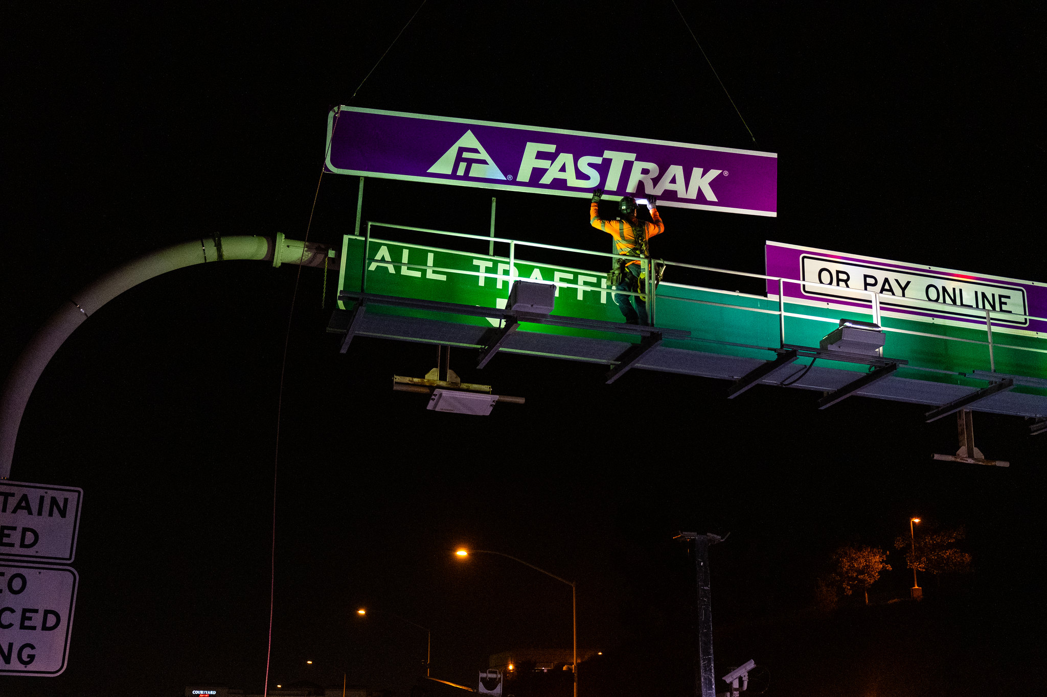 Image of construction crews placing a purple FasTrak sign above the 73 Toll Road