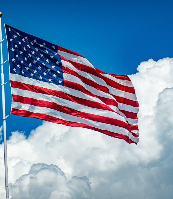 U.S. flag with clouds and blue sky behind it