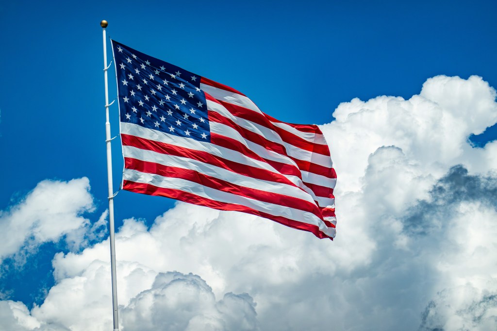 U.S. flag with clouds and blue sky behind it 